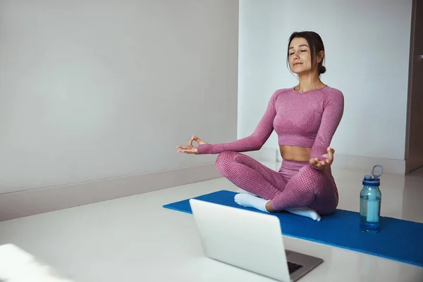 Mulher bonita praticando ioga e usando notebook em casa — Fotografia de Stock