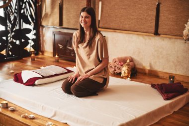 Masaj merkezinde yatağında gülümseyerek oturan memnun bayan.