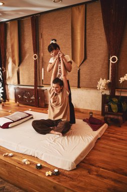 Taylandlı yoga masaj işçisi bayan müşterinin kollarını kaldırıyor.