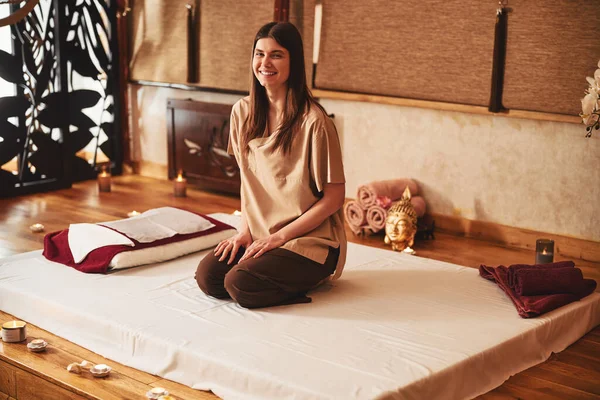 Masaj merkezinde yatağında gülümseyerek oturan memnun bayan.