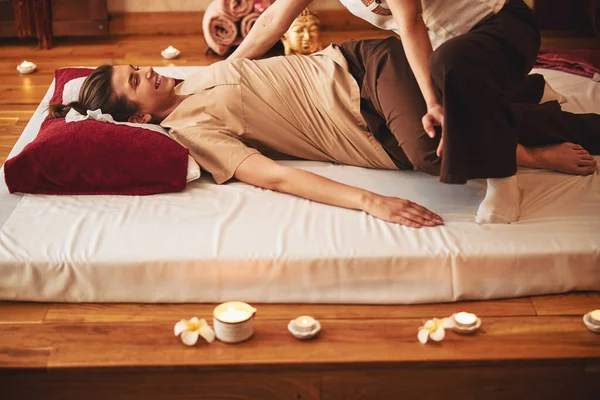 Smiling young woman having legs pressed to bed by masseuse — Stock fotografie