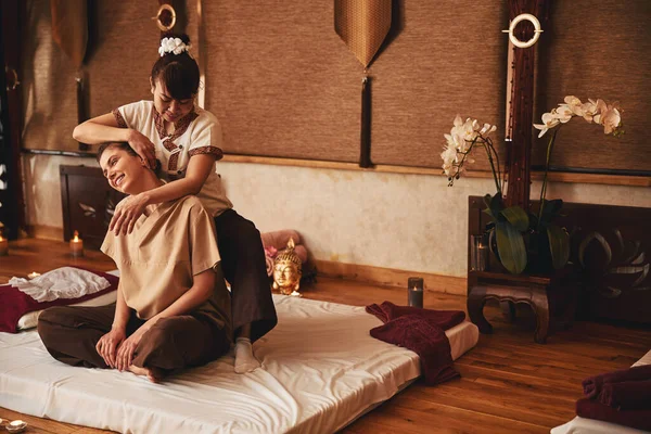 Thai massagist moving her palm along customer ear — Stock fotografie