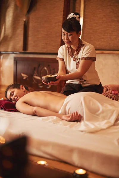 Asyalı masajcı, yağ kabını müşterinin vücudunun üstünde tutuyor. — Stok fotoğraf