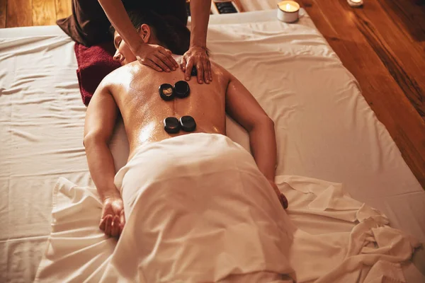 Pessoa massageando fêmea com quatro pedras quentes em suas costas — Fotografia de Stock