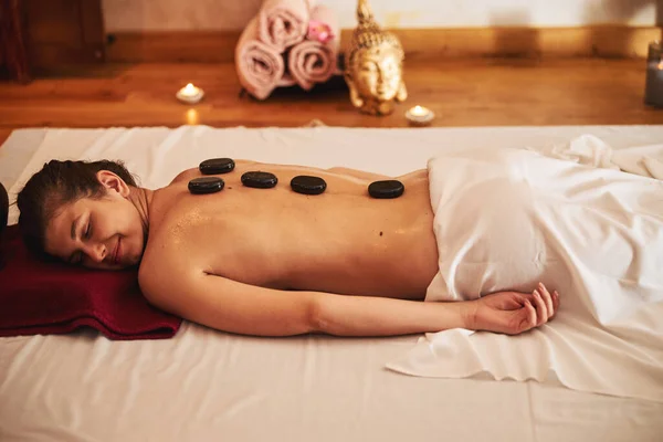 Donna soddisfatta sdraiata con cinque pietre calde sulla schiena — Foto Stock
