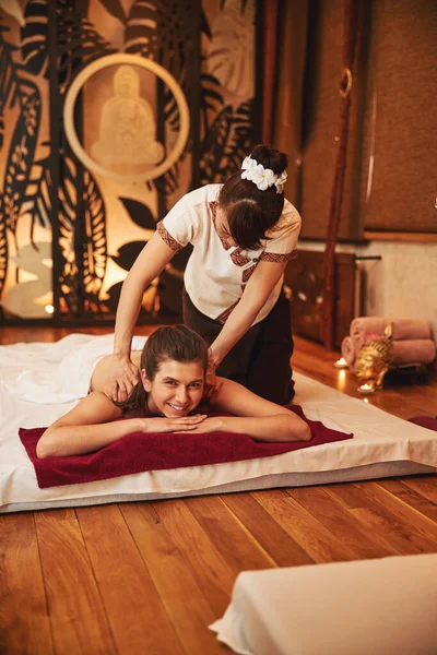Female massage professional kneading shoulders on joyful woman — Stock Photo, Image