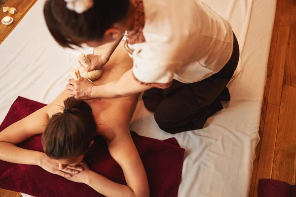 Massagista aplicando cataplasmas de ervas tailandesas na pele do cliente — Fotografia de Stock
