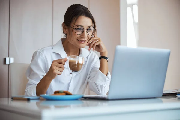 Joyeuse femme d'affaires buvant du latte et utilisant un ordinateur portable au travail — Photo