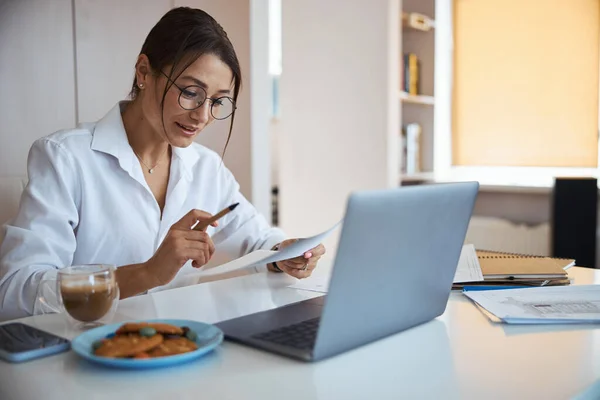 Belle femme étudiant le document et utilisant un ordinateur portable au travail — Photo