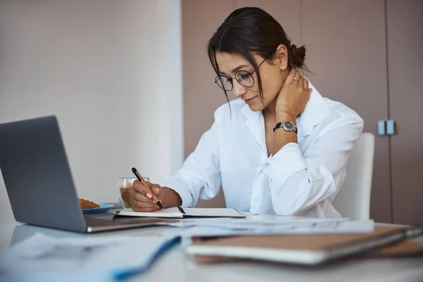 Hermosa mujer escribiendo en el cuaderno y usando el ordenador portátil en el trabajo —  Fotos de Stock