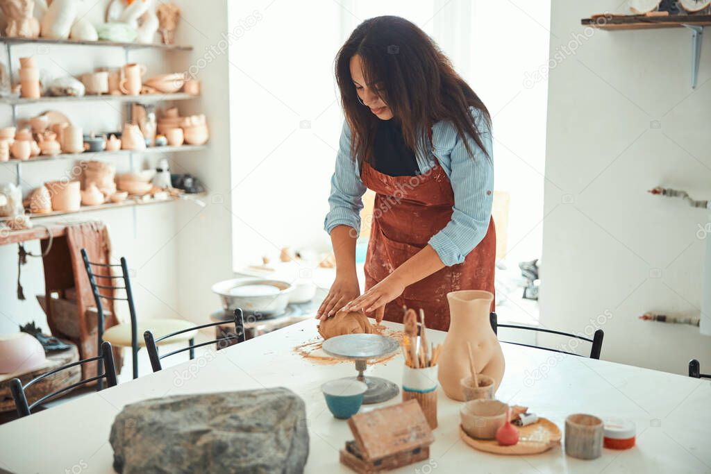 Beautiful woman in apron working in pottery workshop