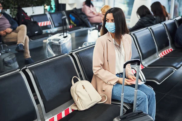 Stílusos nő orvosi maszkban várja a repülést a repülőtéren — Stock Fotó