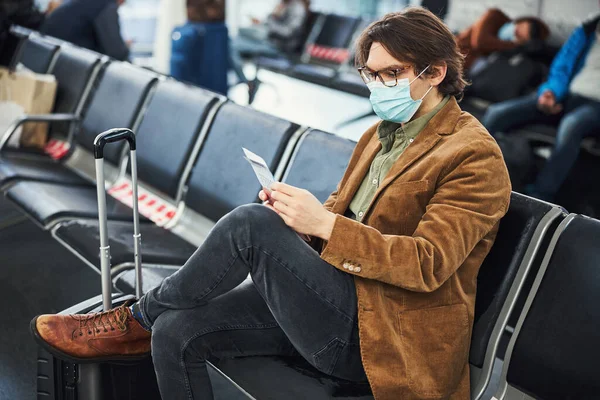 医療マスクのスタイリッシュな男空港で搭乗券をチェック — ストック写真