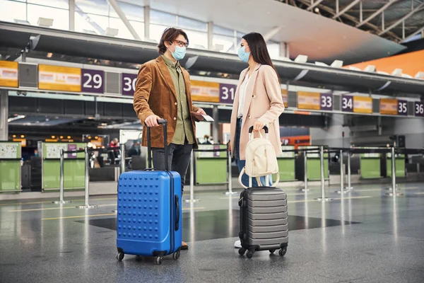 Joven hombre y mujer en máscaras médicas de pie en el aeropuerto —  Fotos de Stock
