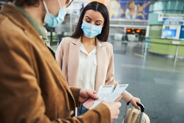 Fiatal nő és férfi orvosi maszkban csekkolja a jegyeket a repülőtéren — Stock Fotó