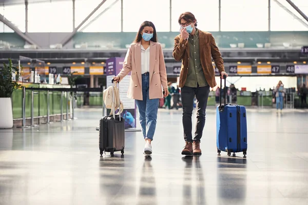 空港ターミナルを歩く顔のマスクの若い男と女 — ストック写真