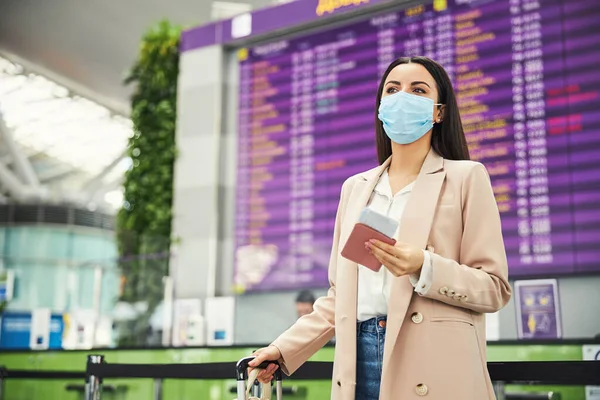 Stílusos nő orvosi maszkban várja a repülést a repülőtéren — Stock Fotó