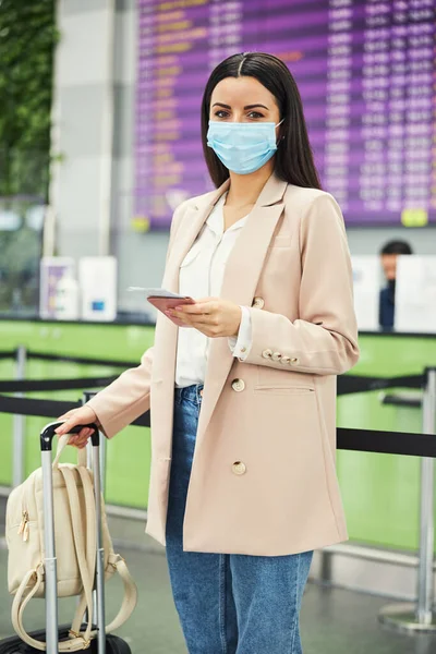 의료용 마스크를 쓴 고상 한 여자 가 공항에서 비행기를 기다리고 있다 — 스톡 사진