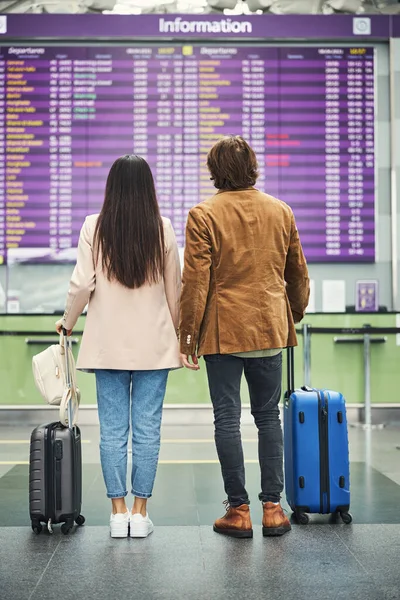 Jóvenes viajeros en pareja mirando a bordo de salida en el aeropuerto — Foto de Stock