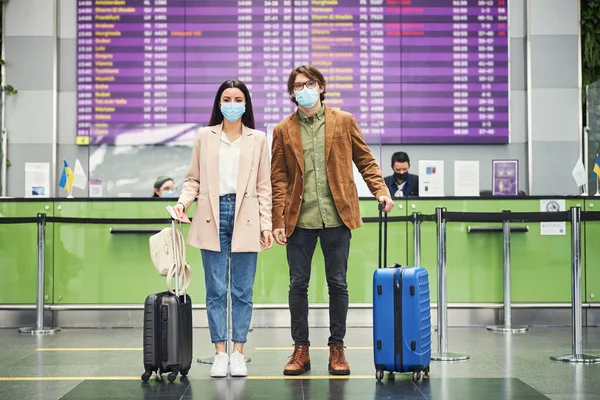 Fiatal pár utazók orvosi maszk áll a repülőtéren — Stock Fotó