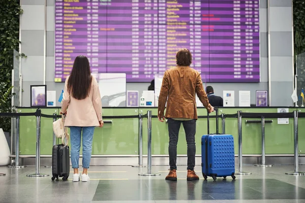 Snygg man och kvinna kontrollerar tiden för planet ankomst till flygplatsen — Stockfoto