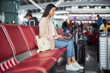 Havaalanı bekleme odasında dizüstü bilgisayar kullanan çekici bir kadın.