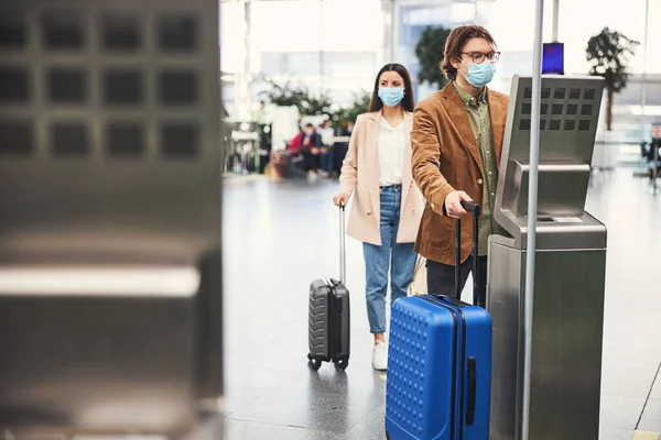 Orvosi maszkos férfi poggyász-ellenőrző mérlegelővel a repülőtéren — Stock Fotó