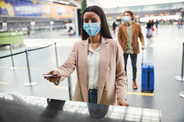 空港のチェックインデスクに立つ医療用マスクのスタイリッシュな女性 — ストック写真