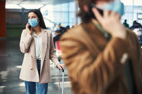 Stílusos nő orvosi maszkban telefonbeszélgetés a repülőtéren — Stock Fotó