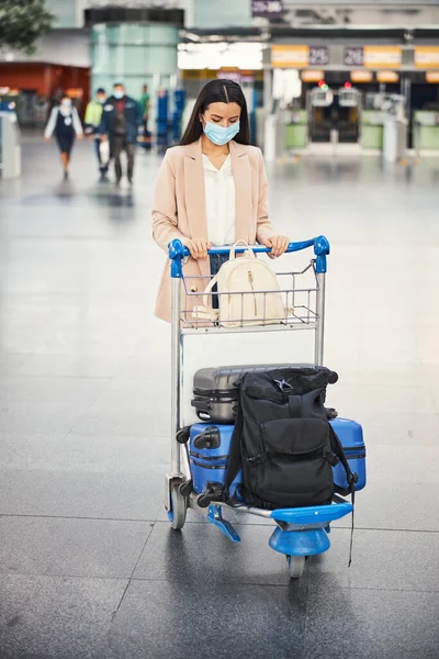 空港で荷物トロリーを押す医療マスクの若い女性 — ストック写真