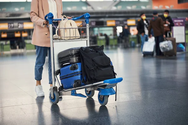 Κομψή νεαρή γυναίκα σπρώχνει αποσκευές τρόλεϊ στο αεροδρόμιο — Φωτογραφία Αρχείου