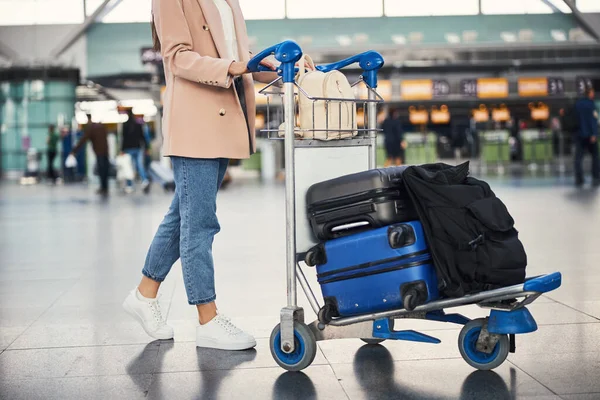 Elegante joven mujer empujando el carrito de equipaje en el aeropuerto —  Fotos de Stock