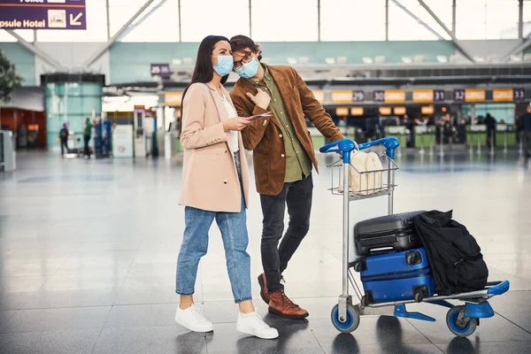 공항 터미널을 걷고 있는 수하물 트롤리를 가진 젊은 부부 — 스톡 사진