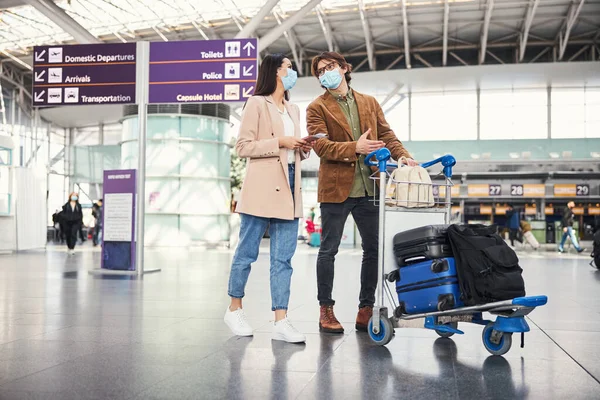 Preciosa pareja con carrito de equipaje caminando por la terminal del aeropuerto —  Fotos de Stock