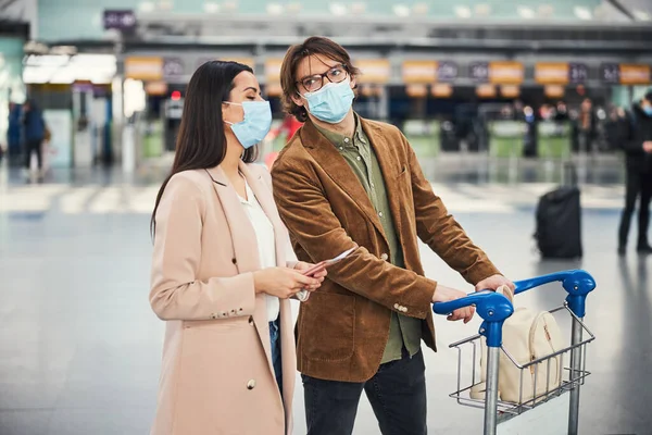 Szép pár orvosi maszkban sétálnak a reptéri terminálon. — Stock Fotó