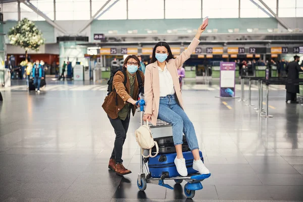 Joven empujando carrito de equipaje con mujer encantadora en el aeropuerto —  Fotos de Stock