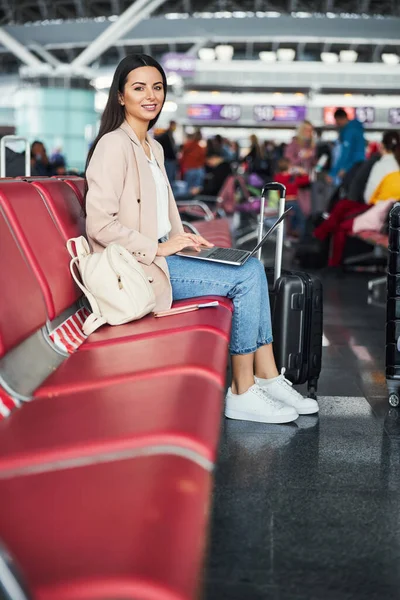 Χαρούμενη γυναίκα που χρησιμοποιεί φορητό υπολογιστή στην αίθουσα αναμονής του αεροδρομίου — Φωτογραφία Αρχείου