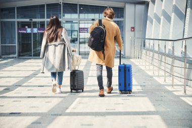Havalimanında seyahat çantası taşıyan şık bir adam ve kadın.