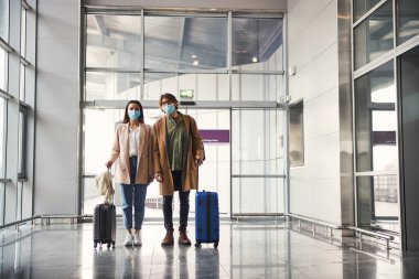 Havalimanı terminalinde maskeli şık bir adam ve kadın duruyor.