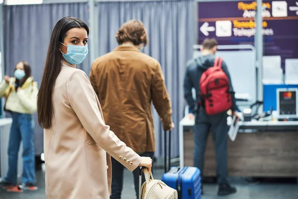 Elbűvölő nő orvosi maszk áll sorban a repülőtéren — Stock Fotó