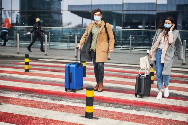 空港の道路を横断する医療マスクの若い女性と男 — ストック写真