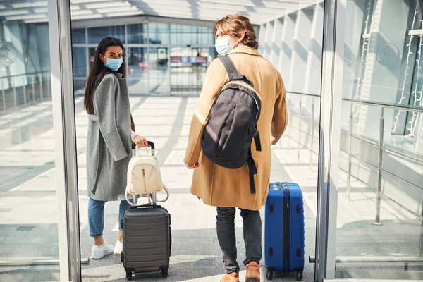 멋진 의료용 마스크를 쓴 멋진 남녀들 이 공항 터미널로 걸어 들어옵니다 — 스톡 사진