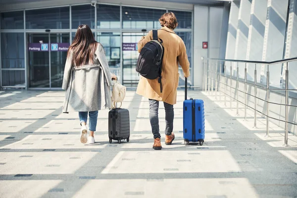 Snygg man och kvinna som bär resväskor på flygplatsen — Stockfoto