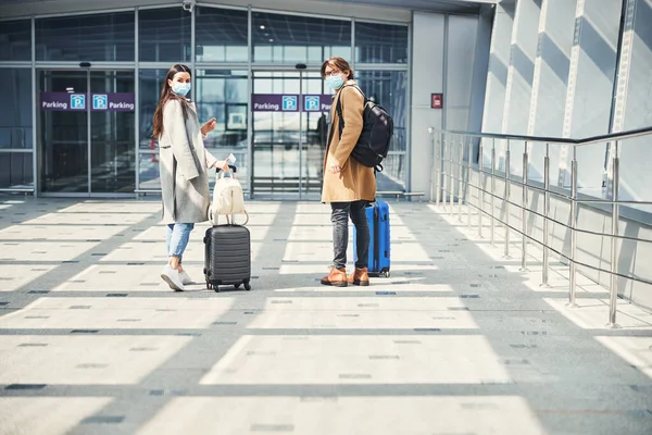 Elegante hombre y mujer en máscaras médicas de pie en el aeropuerto — Foto de Stock