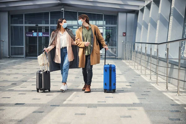 Amar pareja joven en máscaras médicas de pie en el aeropuerto —  Fotos de Stock