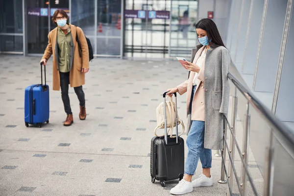 Joven hombre y mujer con máscaras médicas esperando el vuelo en el aeropuerto —  Fotos de Stock