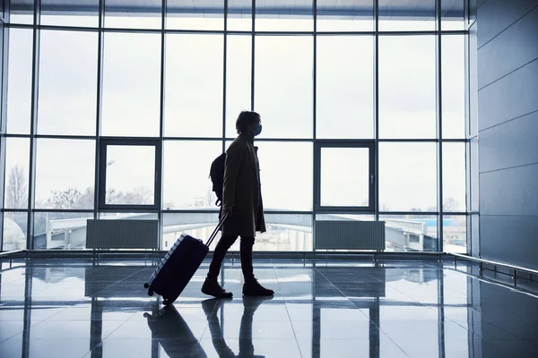 Homem elegante em máscara médica transportando mala de viagem no aeroporto — Fotografia de Stock