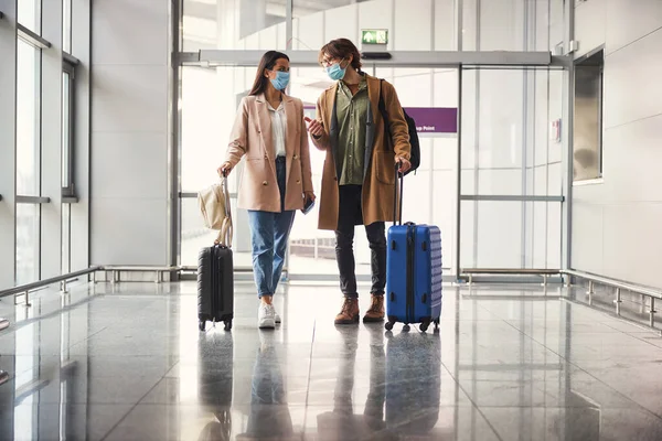 Preciosa pareja joven en máscaras médicas hablando en la terminal del aeropuerto —  Fotos de Stock