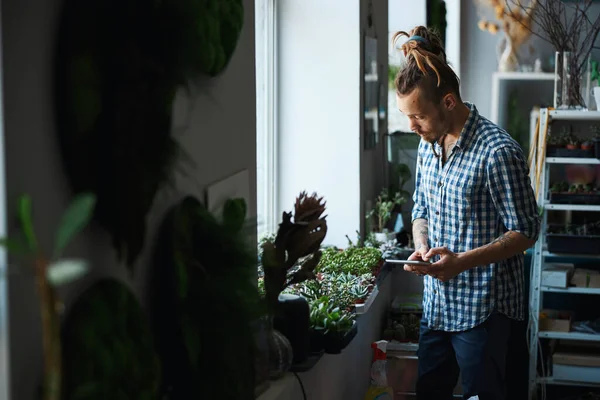 Schöner Mann steht am Fenster und kontrolliert Pflanzen — Stockfoto