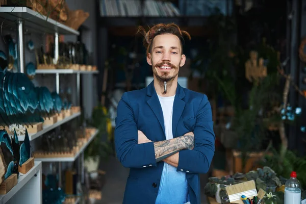 Fröhlicher junger Mann in schicker Jacke steht in Werkstatt — Stockfoto